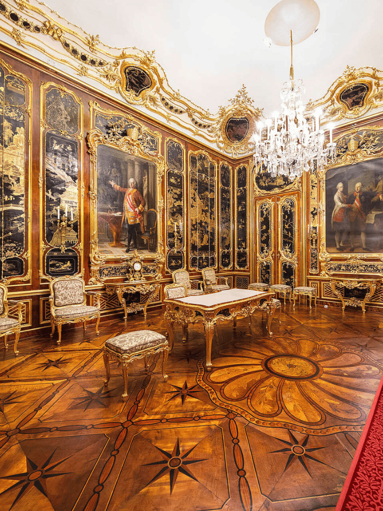Luxurious historic European palace interior with ornate golden decor and grand chandeliers.
