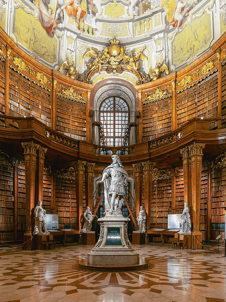 Intricate historic library with ornate woodwork, sculptures, and towering bookshelves in a grand setting.