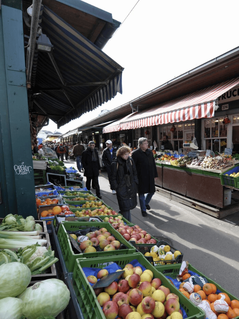 Fresh produce market with apples, vegetables, and shoppers at outdoor vendors.