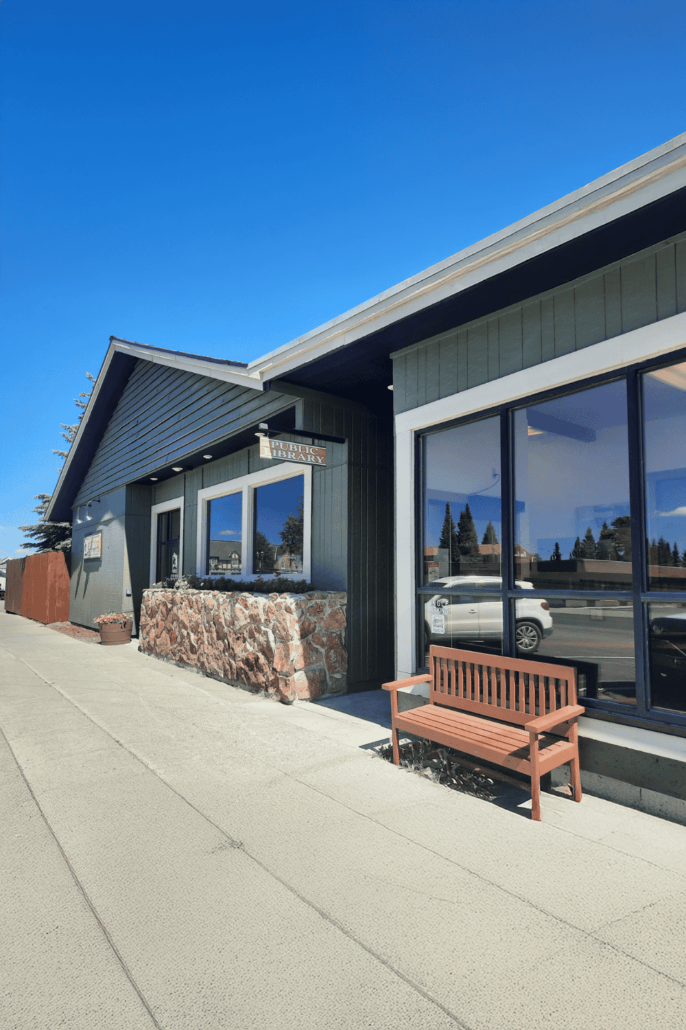 Public Library building exterior with large windows and a bench, located in a community setting.