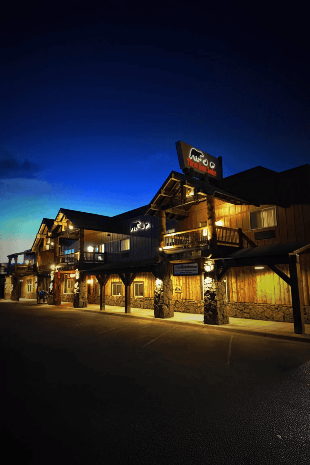 Cozy mountain lodge at night with neon bear sign, outdoor lighting, rustic wood design, and scenic evening sky.