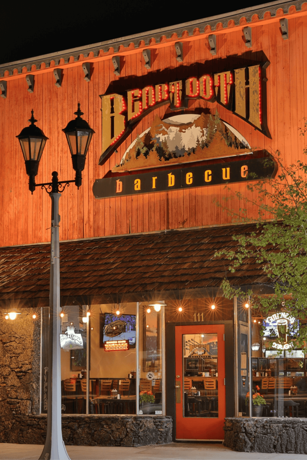 Cozy barbecue restaurant at night with warm lighting, outdoor seating, and rustic wooden exterior.
