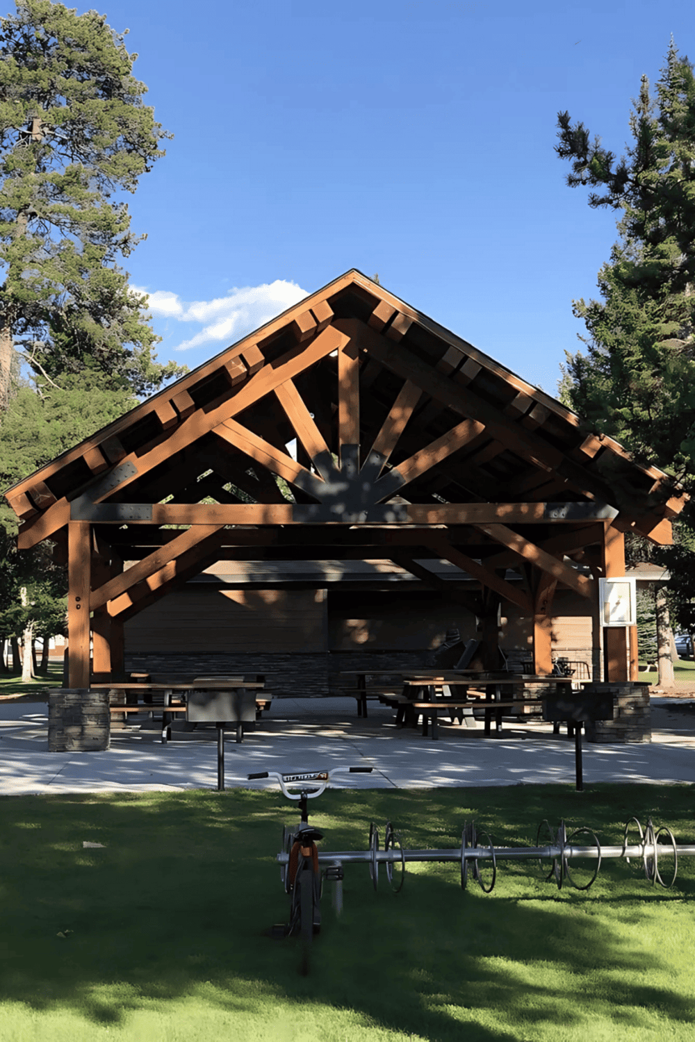 1. Wooden pavilion with picnic tables in a park with tall trees and blue sky.