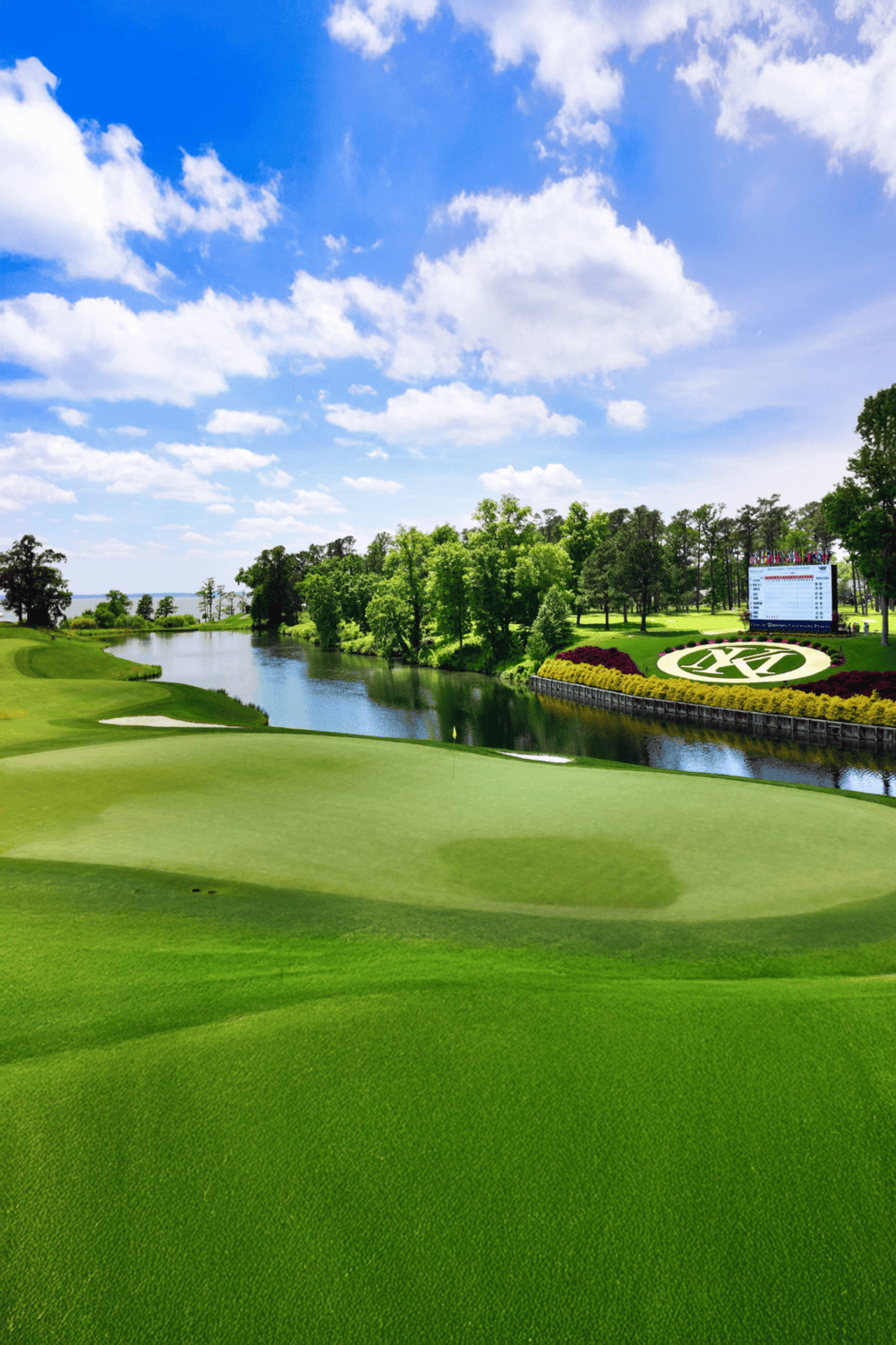 Vibrant golf course with lush green fairways, water hazards, and a scenic backdrop of trees and blue sky.