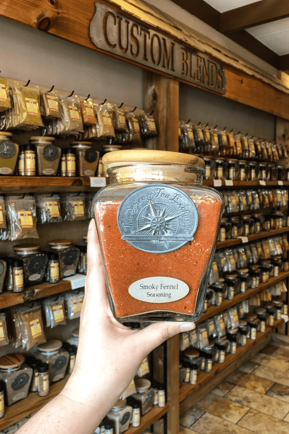 Fresh smoky fennel seasoning in a glass jar at a spice store aisle.