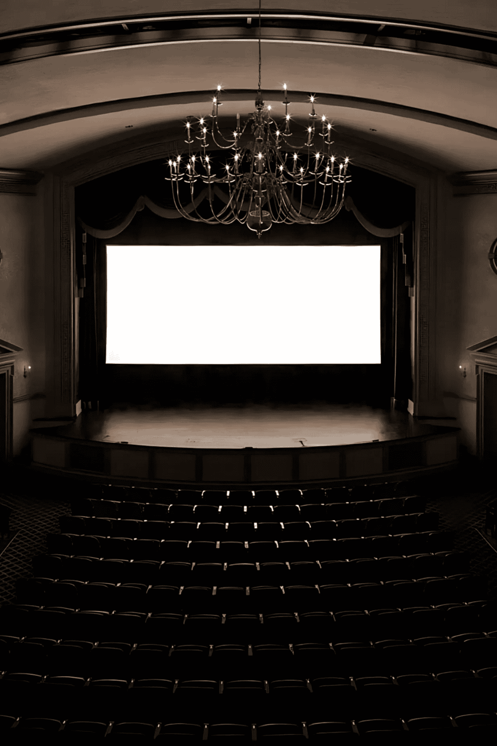 Elegant theater auditorium with large screen, chandelier, and plush seating.