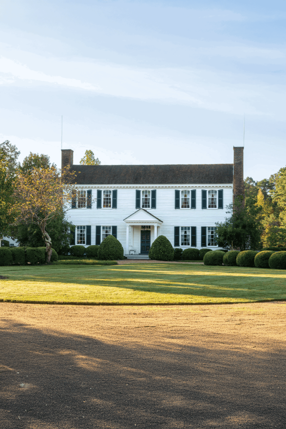 Spacious white historic house with black shutters surrounded by manicured lawn and greenery, national heritage site.