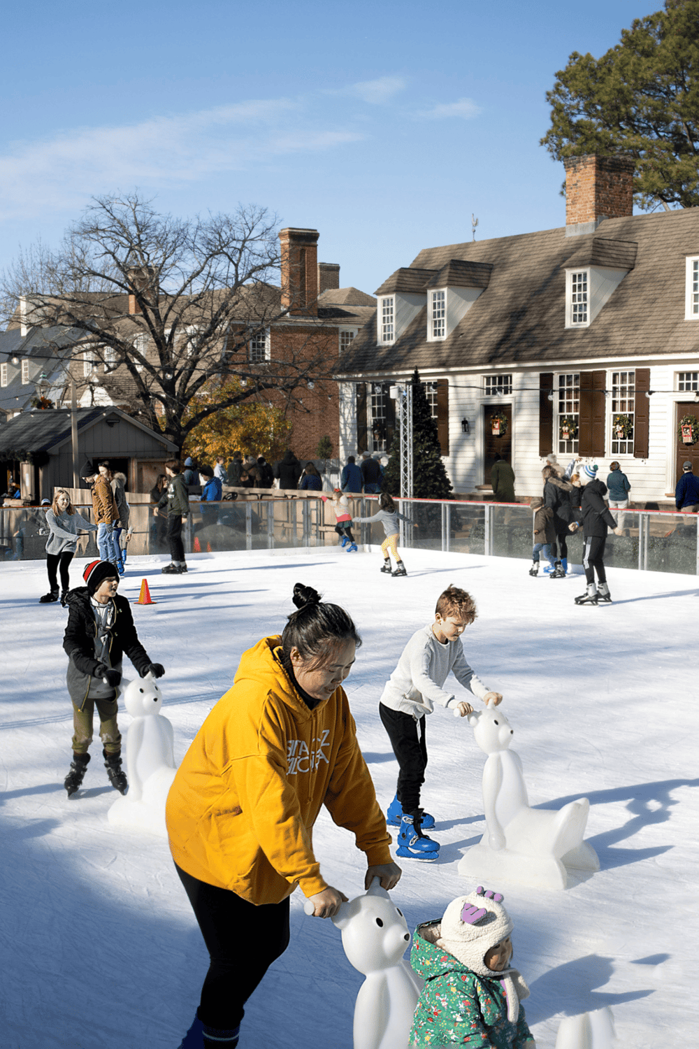 Kids ice skating with snowman sculptures at outdoor rink on winter day.