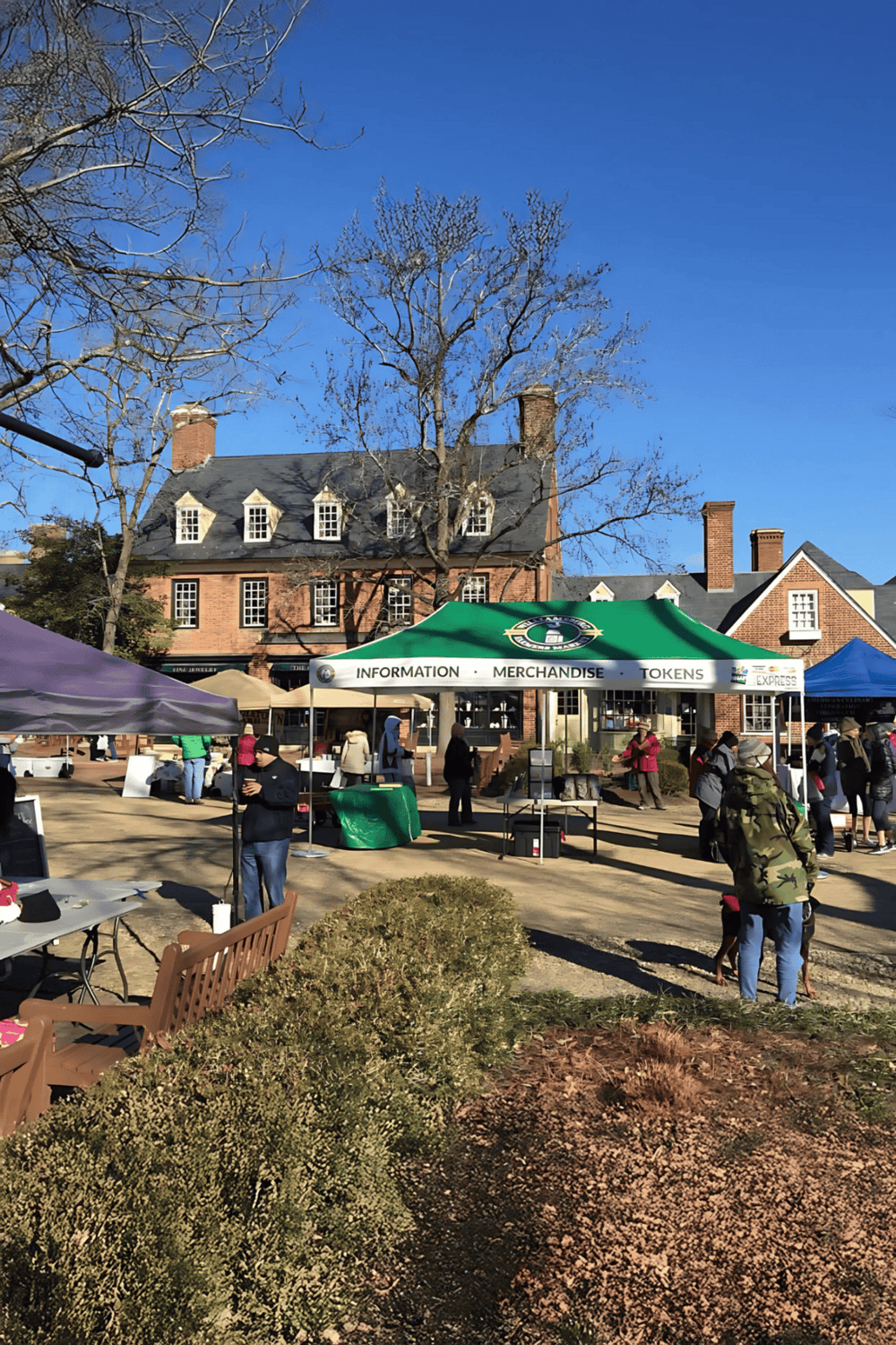 People at outdoor event with QuestForDirections info booth on sunny day.