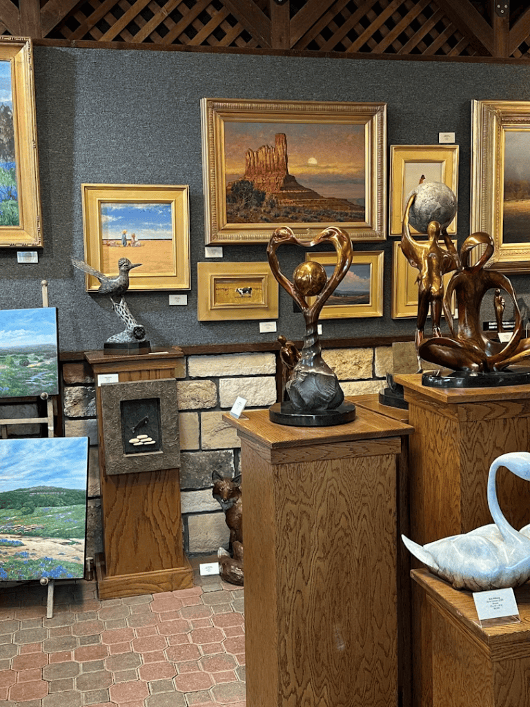 Vibrant art gallery with landscape paintings and bronze sculptures showcasing natural scenery.