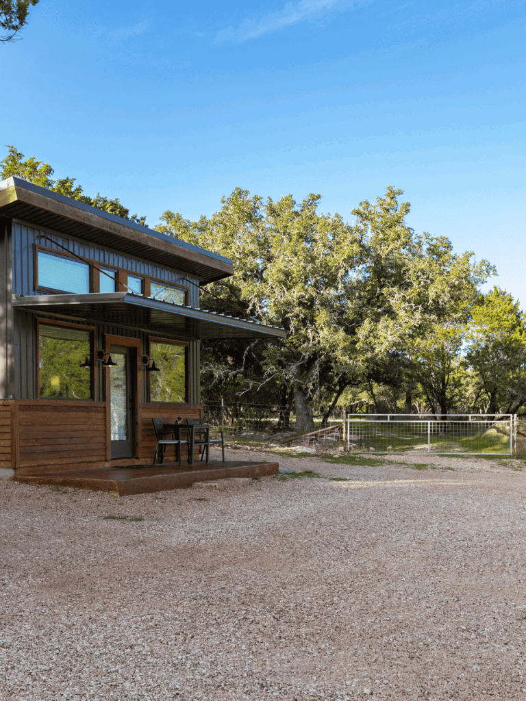 Cozy modern tiny house with large windows surrounded by trees and outdoor seating.