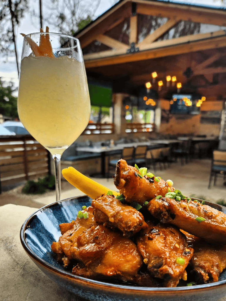 Crispy buffalo chicken wings with lemon wedge and refreshing cocktail in cozy outdoor restaurant setting.