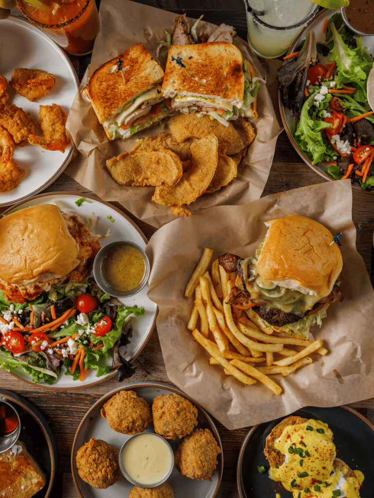 Crispy fried chicken, gourmet burgers, fresh salads, and savory sandwiches served on a rustic wooden table.