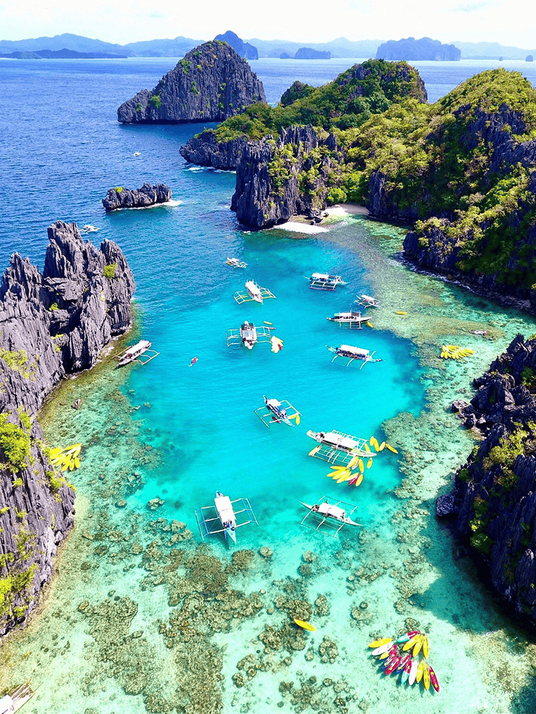 Colorful boats anchored in crystal-clear turquoise waters among limestone cliffs in a tropical island destination.