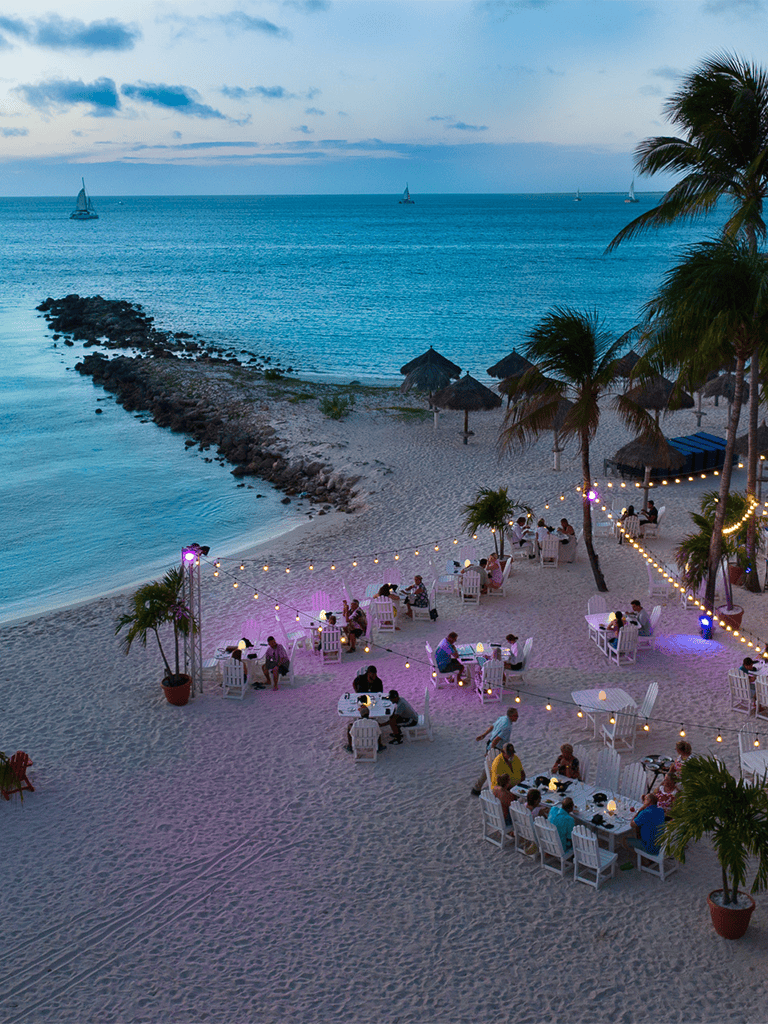 Beachside dining with sunset view and string lights, perfect for relaxation and oceanfront experience.