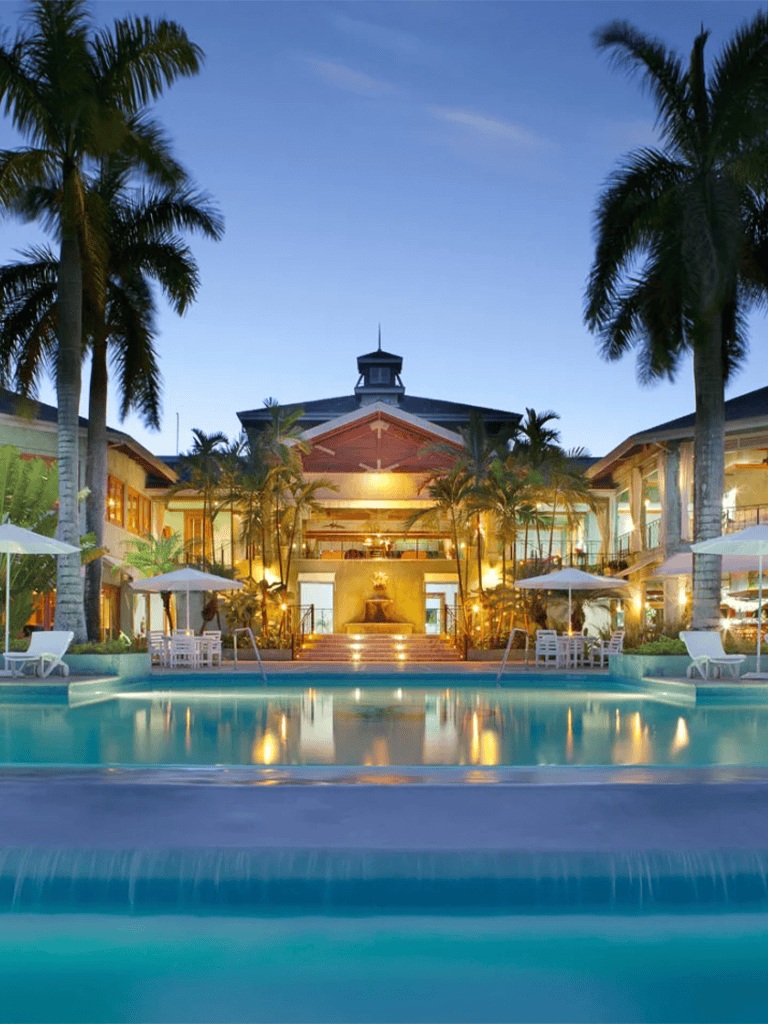 Luxurious tropical resort with swimming pool, palm trees, and elegant architecture at sunset.