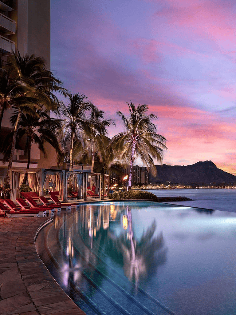 Relaxing beachfront pool at sunset with palm trees and mountain view, perfect for vacation and travel planning.