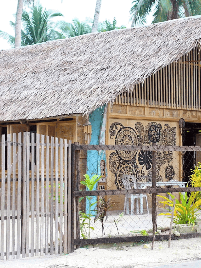 Colorful tropical hut with thatched roof and traditional wall art, surrounded by lush greenery.