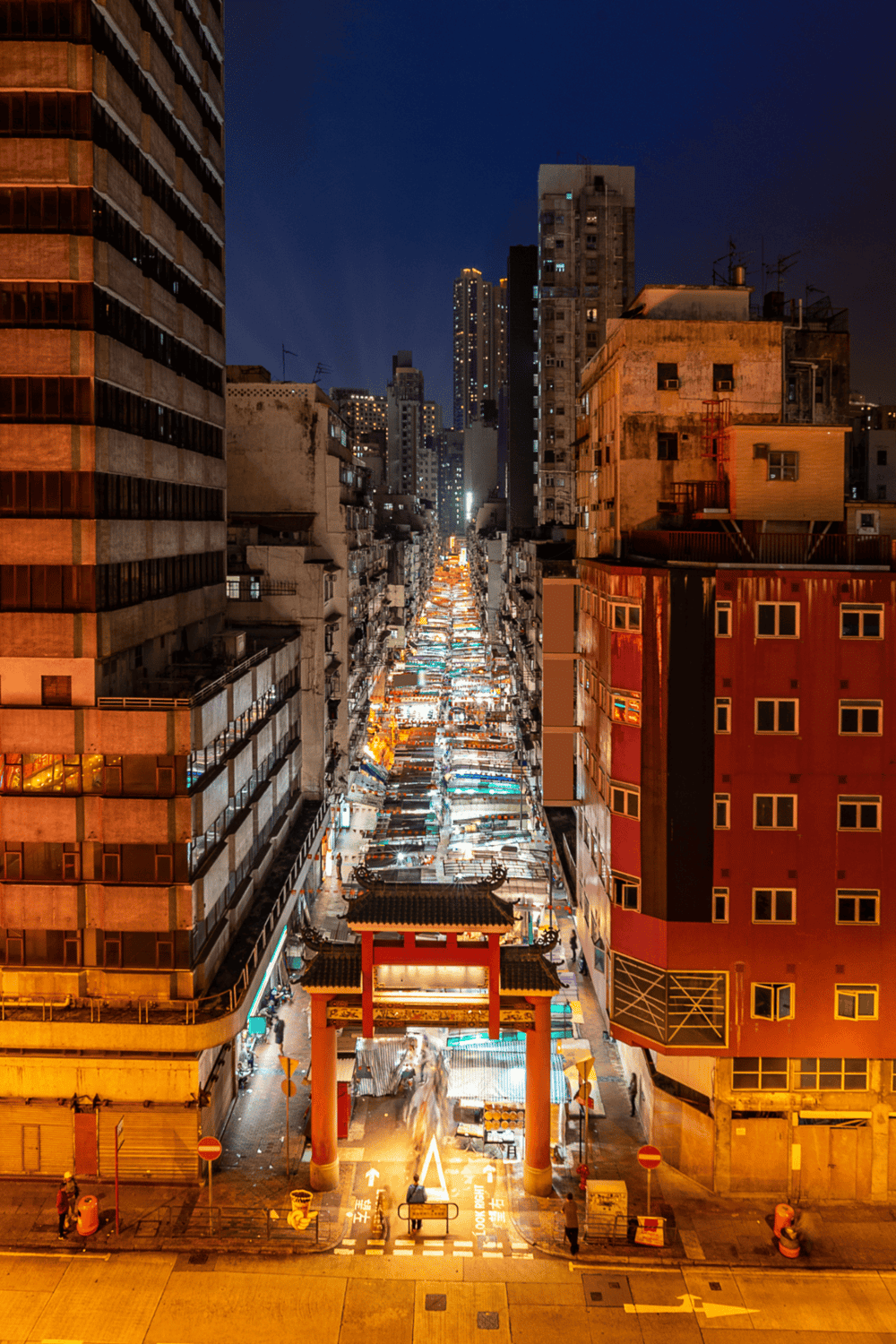 Modern urban street at night with vibrant city lights and a traditional Asian gate entrance.