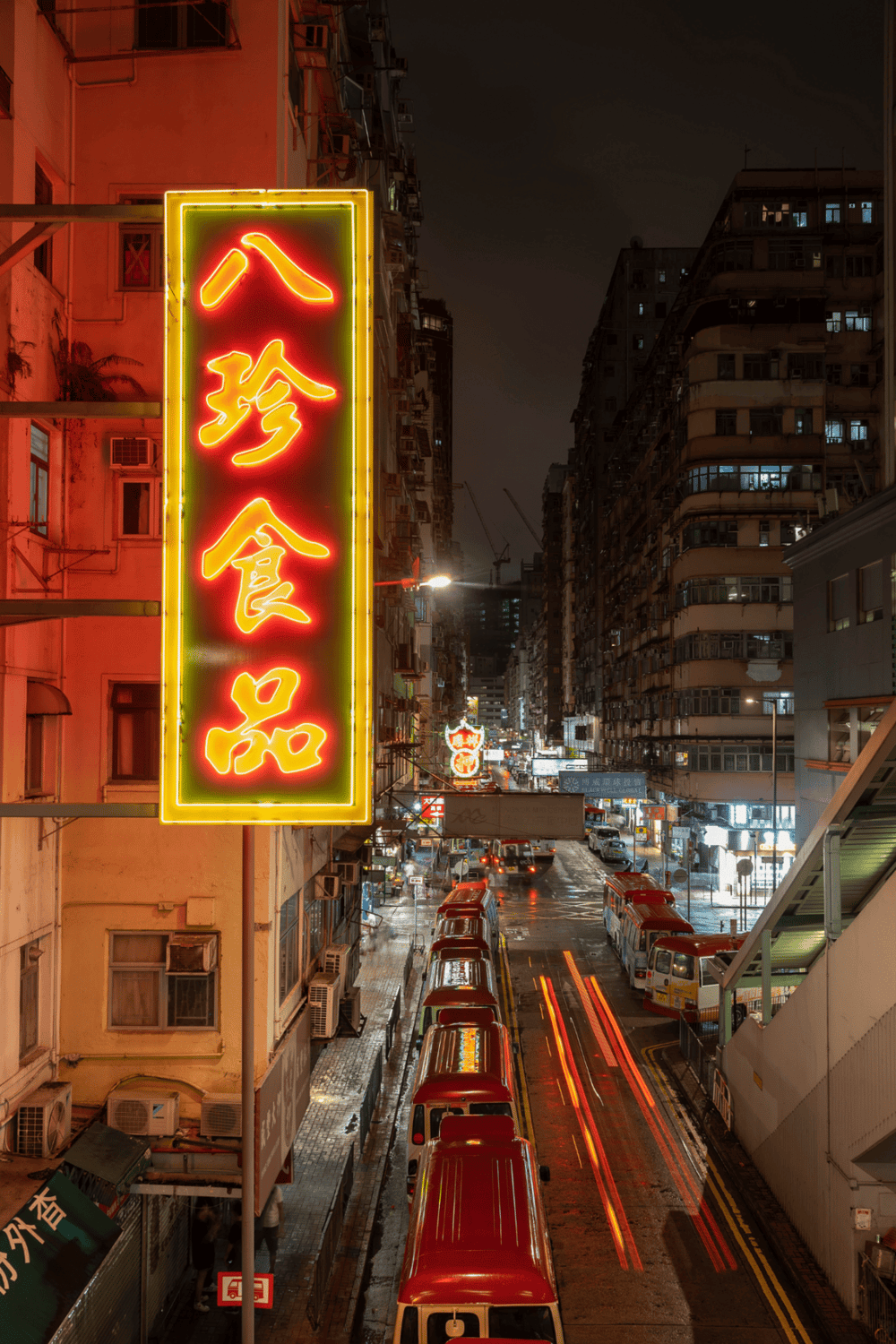 Neon Chinese restaurant sign in a busy night city street with tall apartment buildings and red taxis.