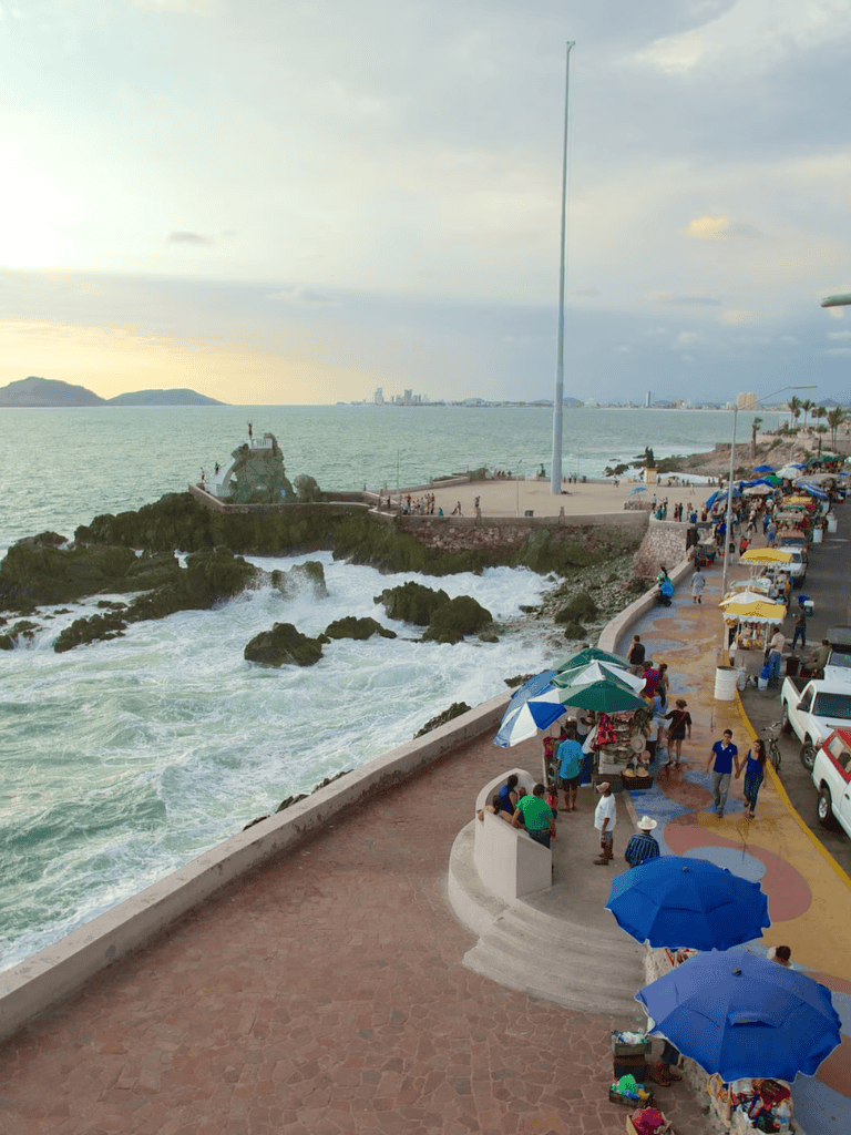 Vibrant seaside scene with waves crashing and colorful market stalls in a coastal town.