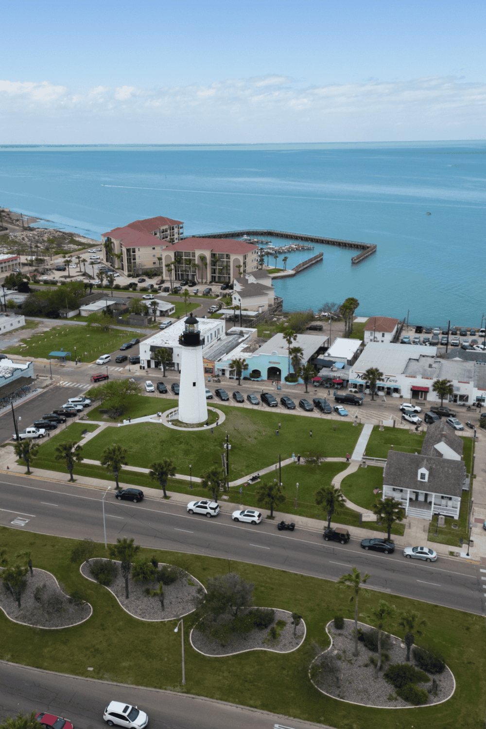 Aerial view of a coastal town featuring a lighthouse, marina, and ocean horizon, perfect for welcoming travelers and boat enthusiasts.