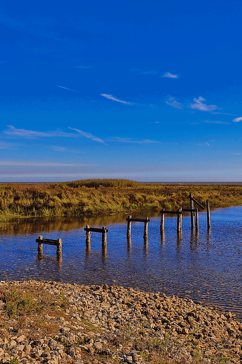 Old wooden pier on a calm water body with grassy landscape and blue sky, promoting travel and navigation from QuestForDirections.