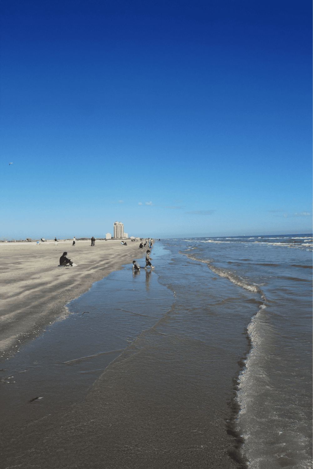 Seaside beach with families and children enjoying the shoreline, featuring clear blue skies and ocean waves for travel inspiration.