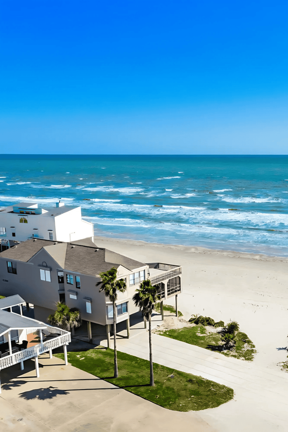 Stunning beach house by the ocean with palm trees and clear blue skies, perfect for seaside vacation rentals.