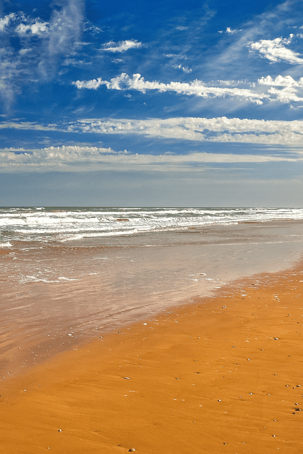 Vast ocean beach with blue sky and white clouds, scenic coastal view for travel or relaxation.