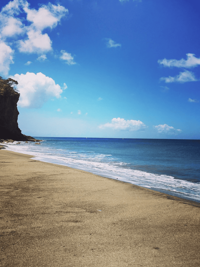 Serene beach scene with sand, ocean waves, and a blue sky with clouds, ideal for travel and vacation planning.