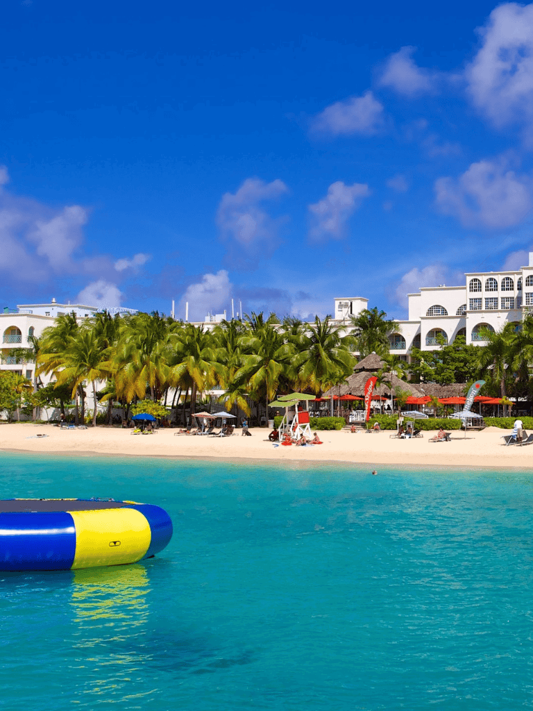 Tropical beach with white hotels, palm trees, and clear turquoise water in the Caribbean.