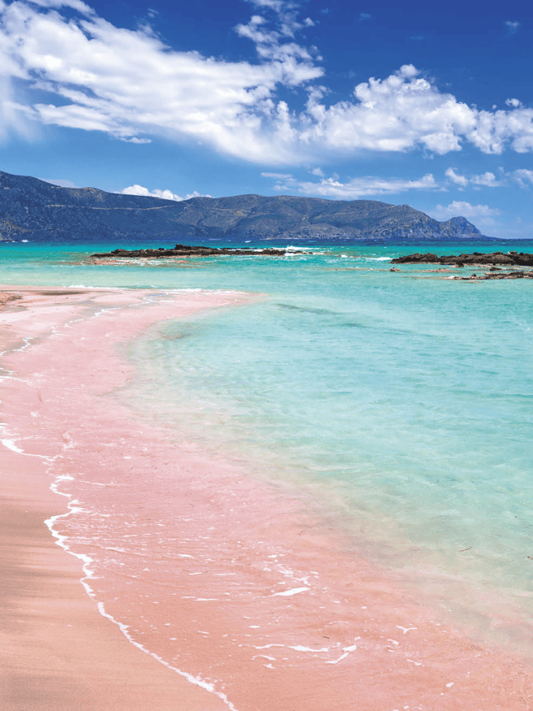 Tranquil pink sandy beach with turquoise waters and mountain backdrop, perfect for travel planning.