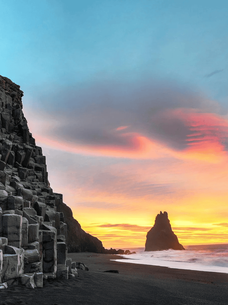 Aerial view of Reynisfjara black sand beach in Iceland during sunset, showcasing basalt stacks and ocean waves.