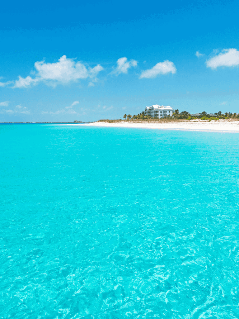 Turquoise ocean with clear water and a distant hotel on a tropical beach.