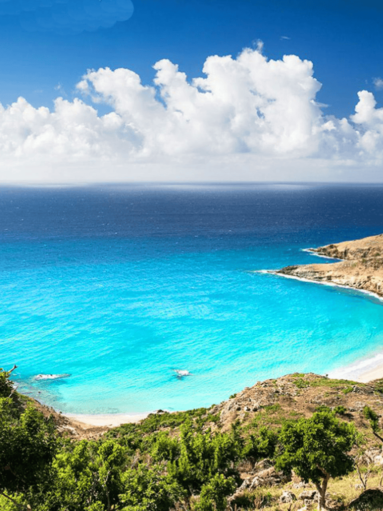 Stunning coastal view with turquoise water and lush green hills under a bright blue sky.
