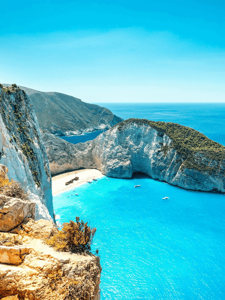 Breathtaking view of Navagio Beach with turquoise waters, cliffs, and clear blue sky on Zakynthos, Greece.