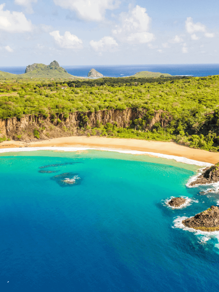 Pristine tropical beach with turquoise waters and lush green cliffs on a sunny day.