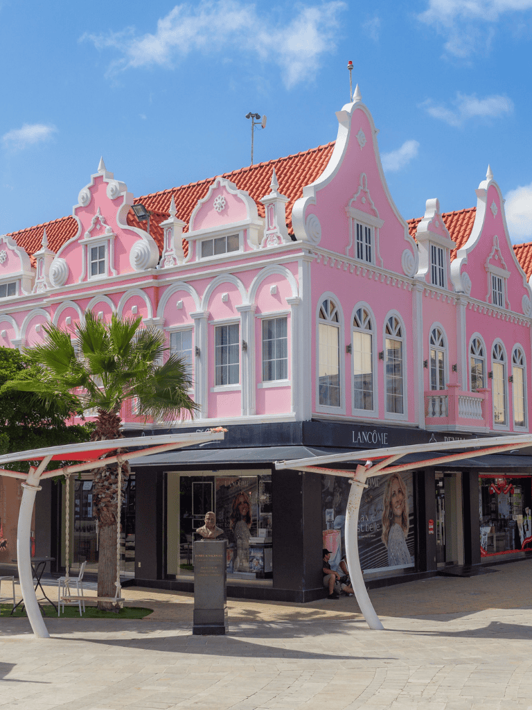 Pink Victorian-style building with storefronts, palm tree, and sunny sky.