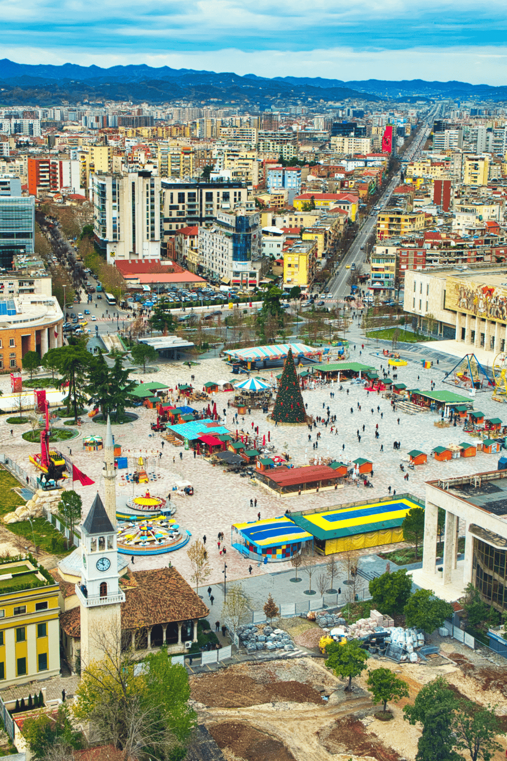 Aerial view of an urban city with a festive Christmas market, colorful stalls, and a decorated tree in downtown area.