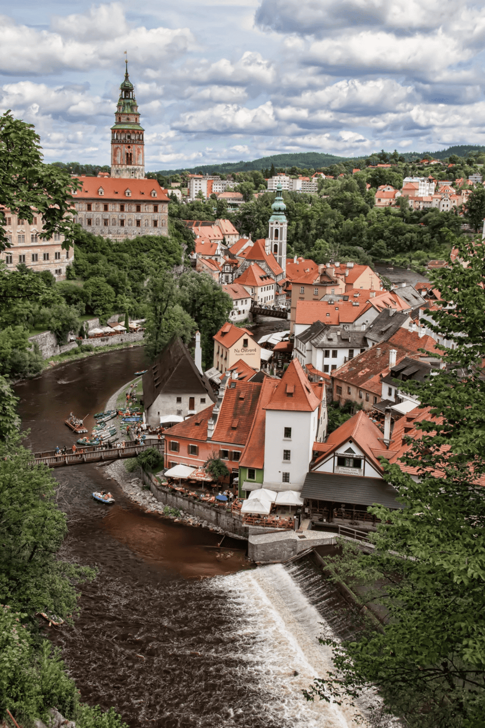 Ancient European town with red rooftops and a river, scenic view of historic architecture and lush greenery.