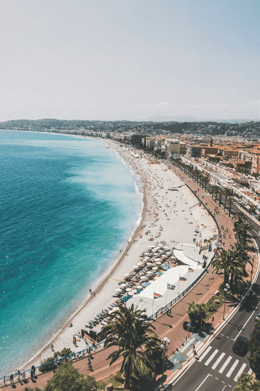 Panoramic view of a coastal beach with palm trees and a bustling boardwalk in a popular travel destination.