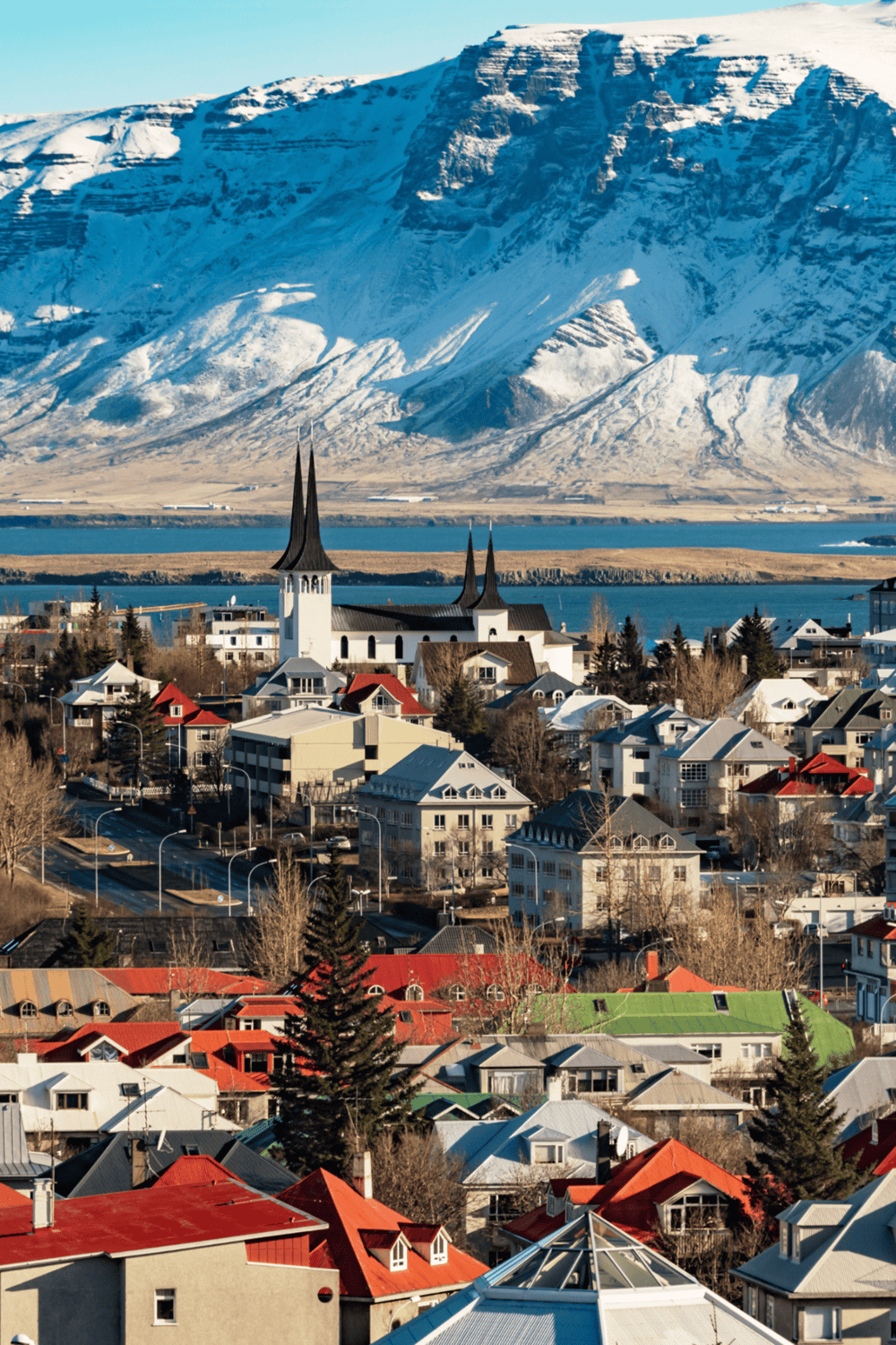 Snow-capped mountains and charming townscape in Iceland, with colorful houses and iconic steeple church.