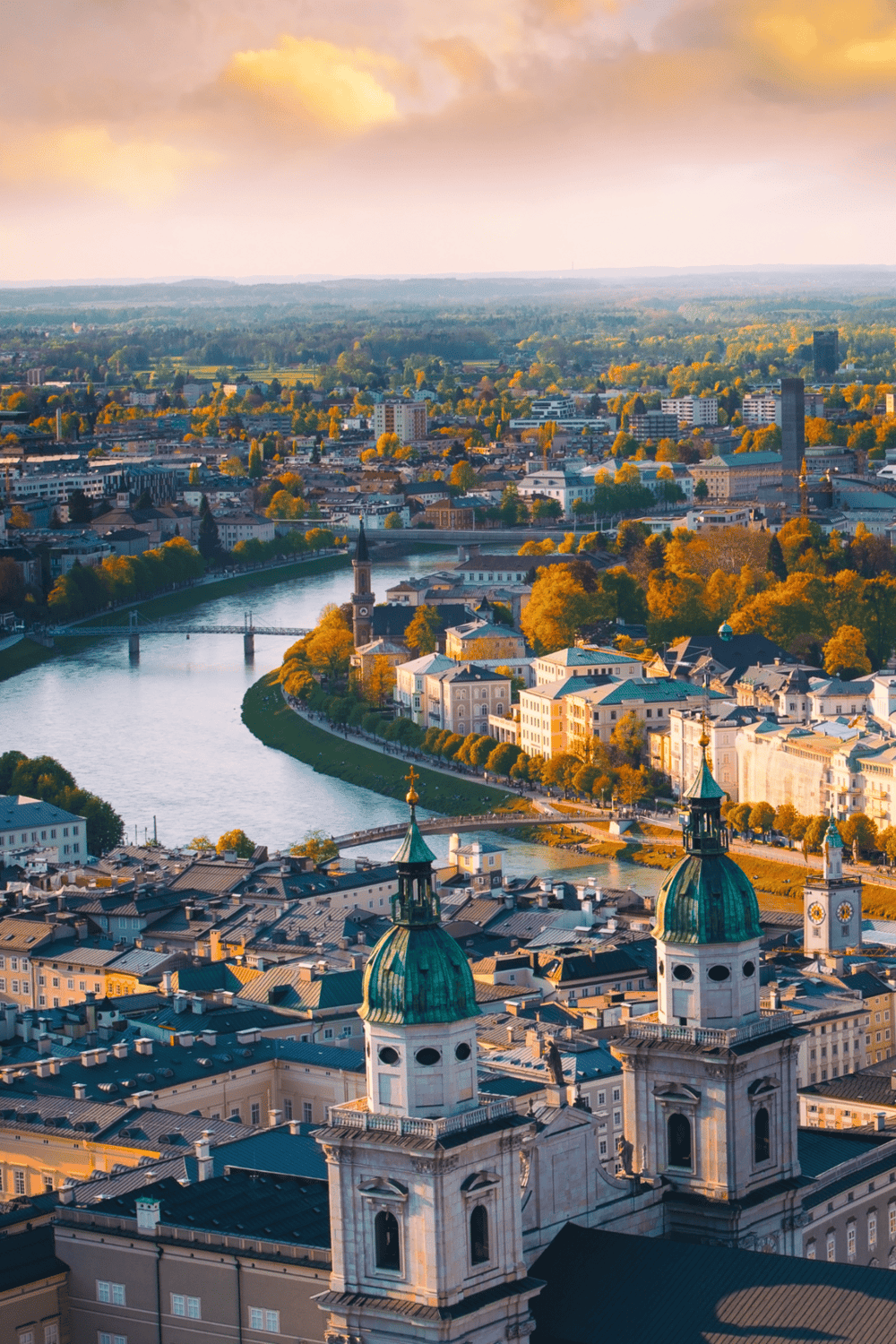 View of a city skyline with historic churches and a river in the foreground, captured during sunset.