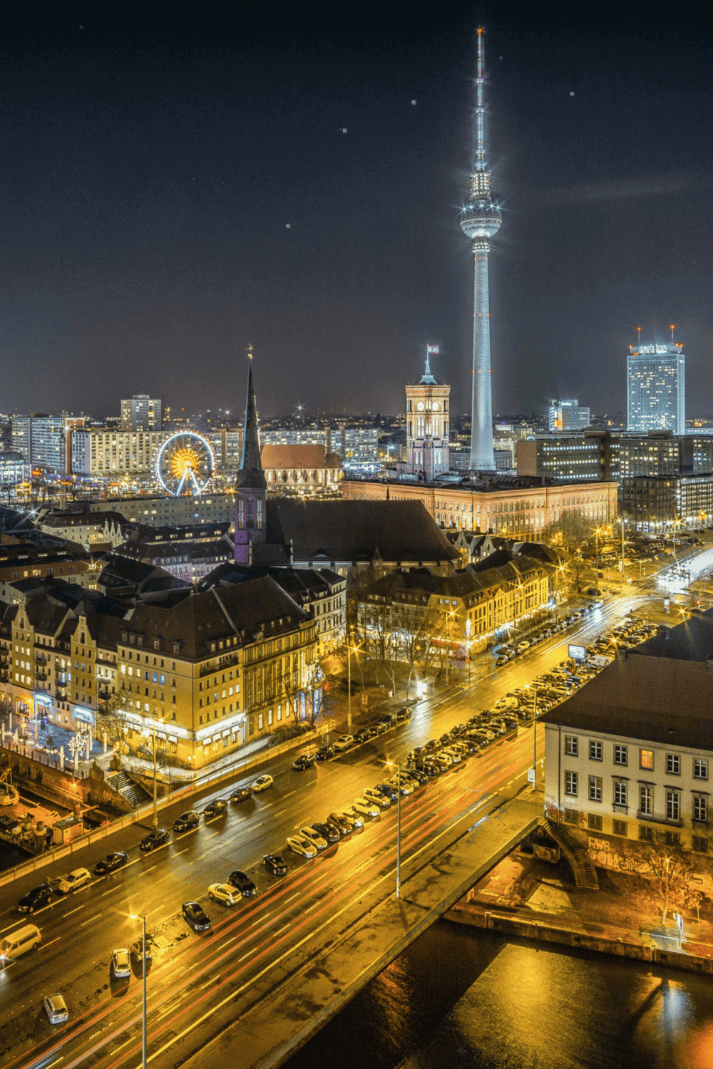 Night skyline of Berlin with TV Tower, illuminated historic buildings, and busy streets.
