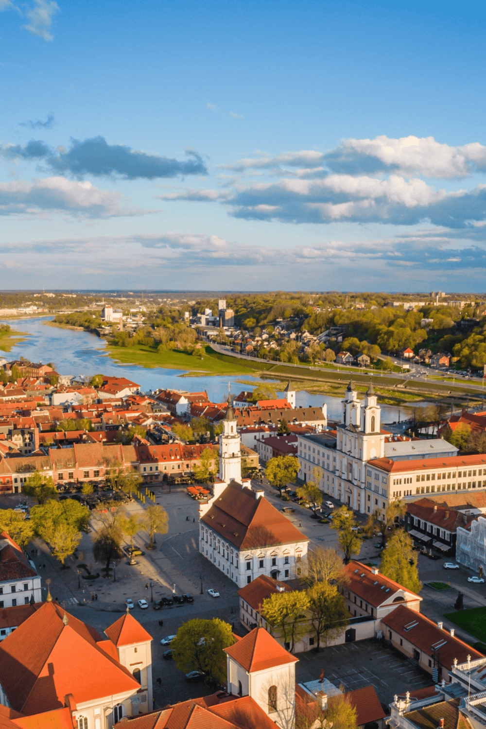 Colorful aerial view of a historic town with a river, churches, and lush greenery, showcasing a vibrant travel destination.