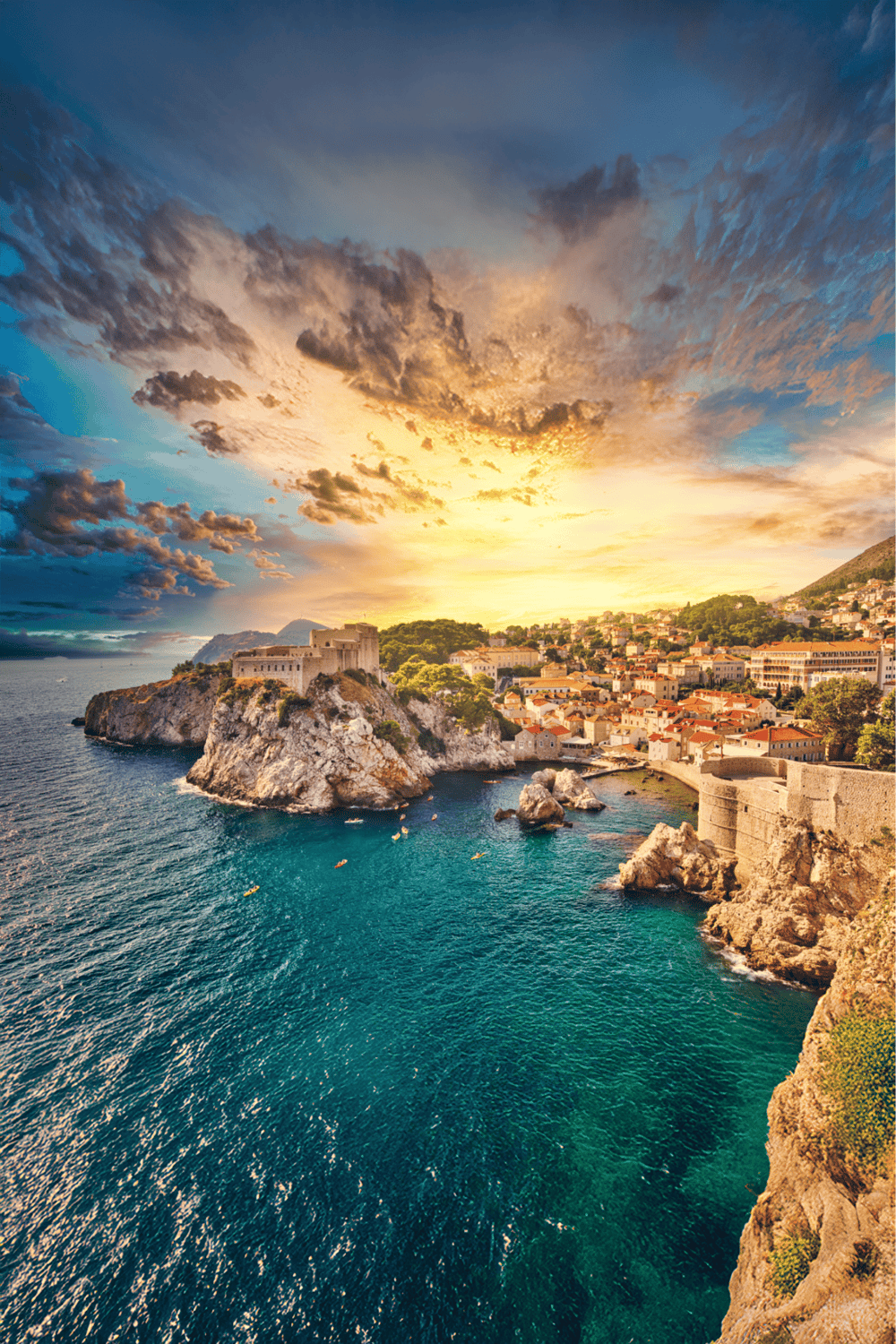 Vibrant sunset over seaside town with historic castle and colorful houses on rocky coast.