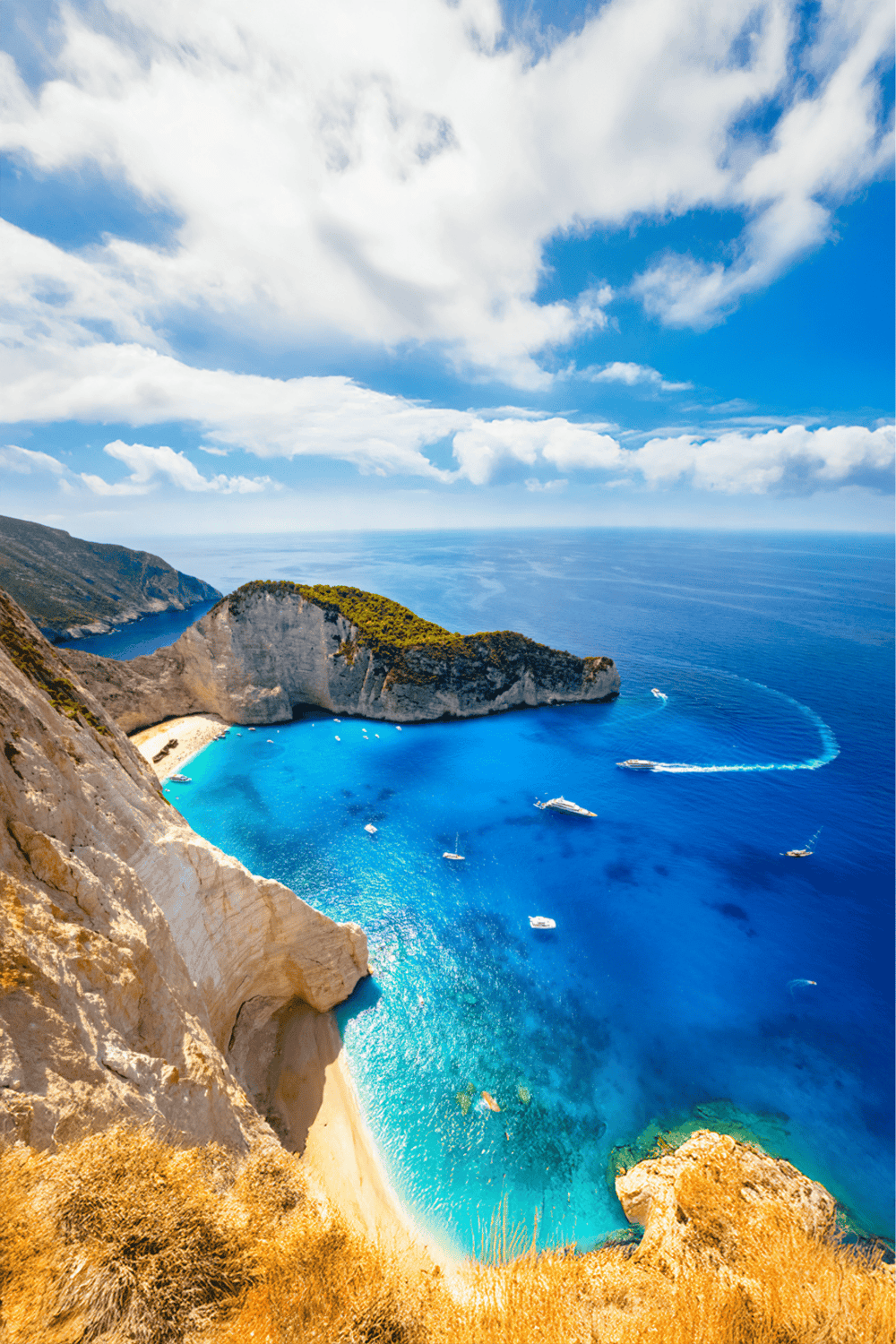 Stunning coastal cliffs and turquoise waters at Navagio Beach, Greece with boats and scenic sky.