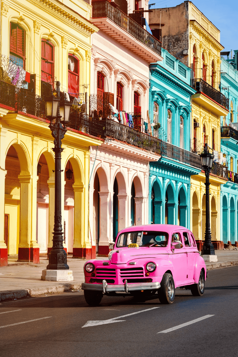 Colorful colonial buildings in Havana with vintage pink taxi in Cuba, popular tourist destination.