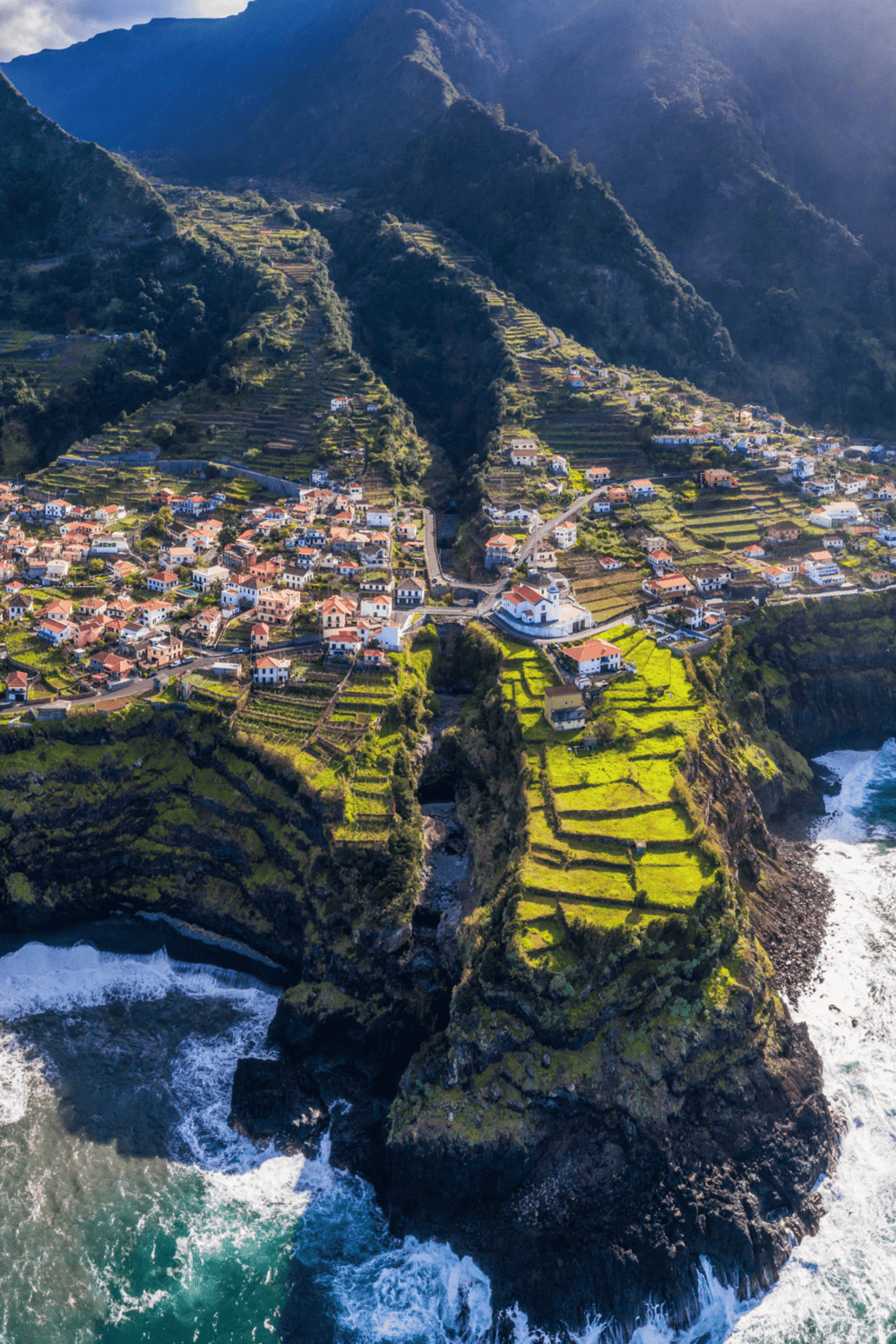 Highland coastal village with terraced fields and colorful houses overlooking the ocean.